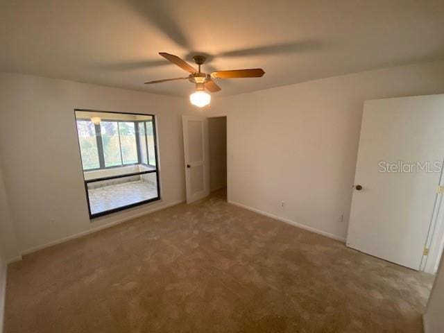 carpeted spare room with a ceiling fan and baseboards