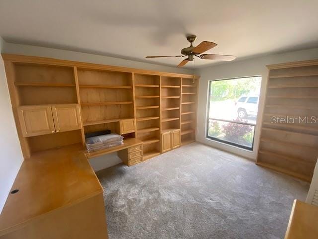 unfurnished office with carpet floors, a ceiling fan, and built in desk