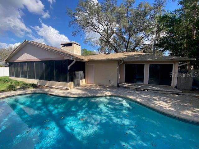 rear view of house featuring an outdoor pool, a sunroom, stucco siding, a chimney, and a patio area