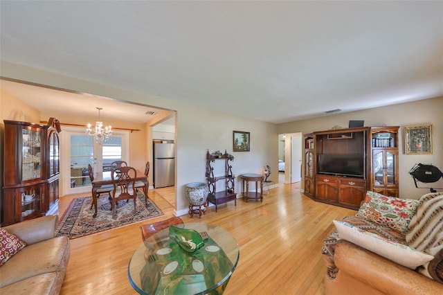 living area with an inviting chandelier, light wood-style flooring, visible vents, and baseboards