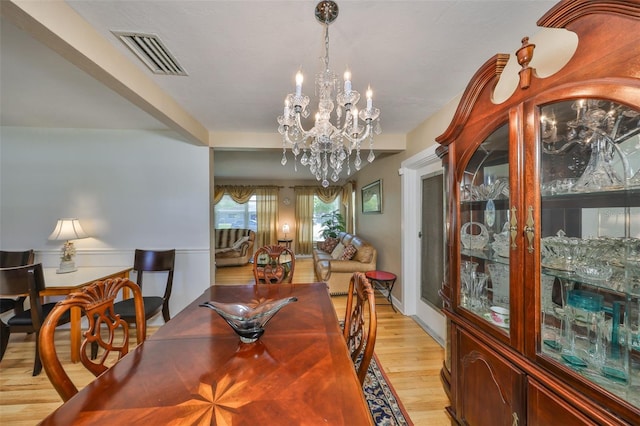 dining area featuring light wood finished floors, visible vents, and an inviting chandelier