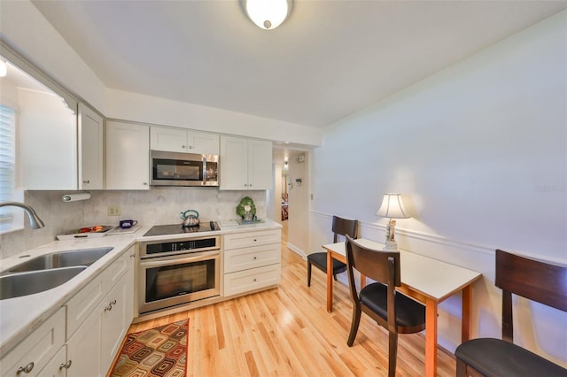 kitchen featuring light countertops, decorative backsplash, appliances with stainless steel finishes, light wood-style floors, and a sink