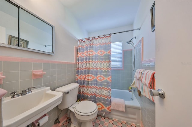 bathroom featuring toilet, a wainscoted wall, a sink, shower / bathtub combination with curtain, and tile walls