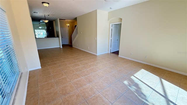 spare room featuring baseboards, a ceiling fan, arched walkways, and light tile patterned floors