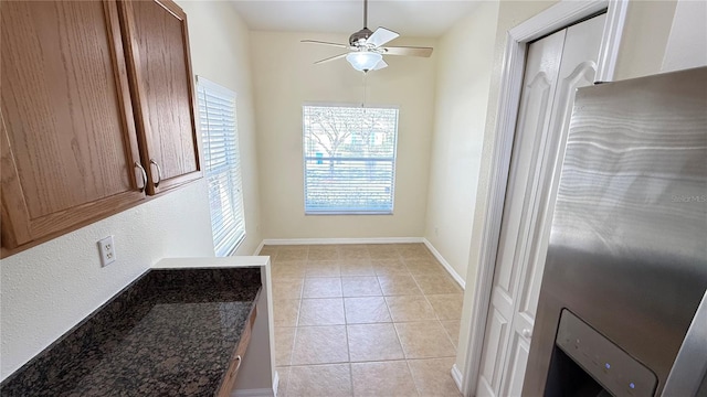 kitchen with dark stone counters, light tile patterned flooring, baseboards, and ceiling fan