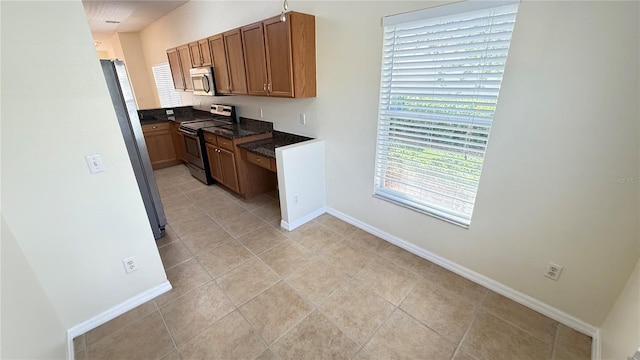kitchen featuring baseboards, brown cabinets, appliances with stainless steel finishes, and light tile patterned floors