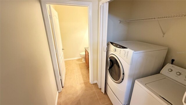 clothes washing area with light tile patterned floors, baseboards, and separate washer and dryer