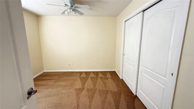 unfurnished bedroom featuring baseboards, a textured ceiling, carpet floors, a ceiling fan, and a closet