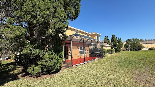 back of property featuring stucco siding, glass enclosure, and a yard