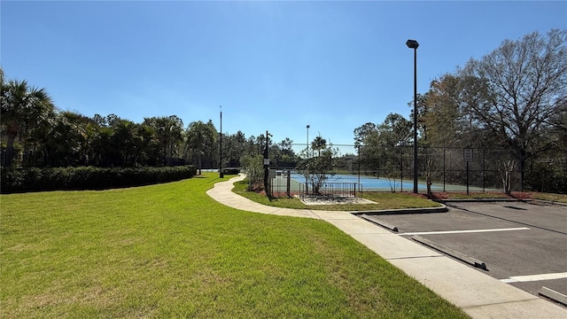 view of home's community with a water view, fence, a tennis court, uncovered parking, and a yard