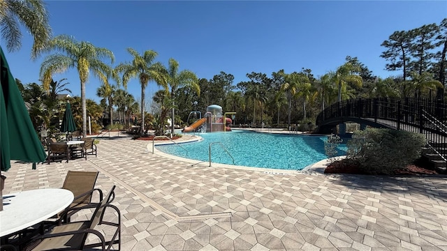 community pool featuring fence, playground community, a water slide, and a patio area