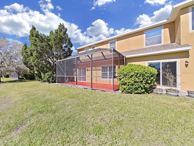 back of house with stucco siding, a yard, and a lanai