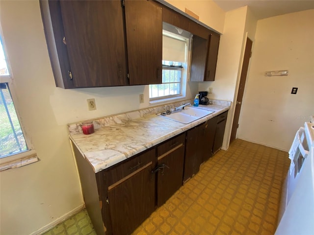 kitchen featuring light floors, light countertops, dark brown cabinetry, a sink, and baseboards