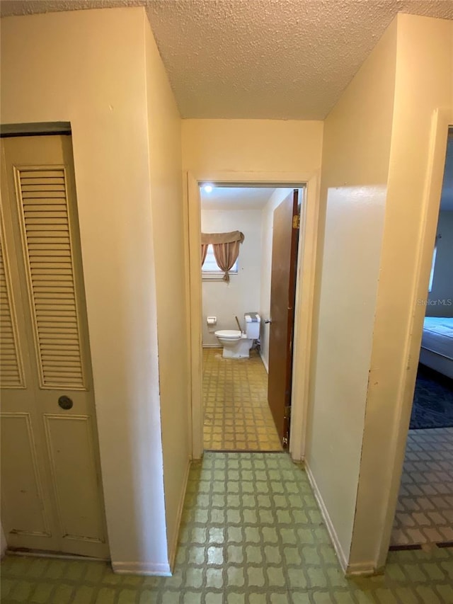 corridor featuring baseboards, a textured ceiling, and tile patterned floors