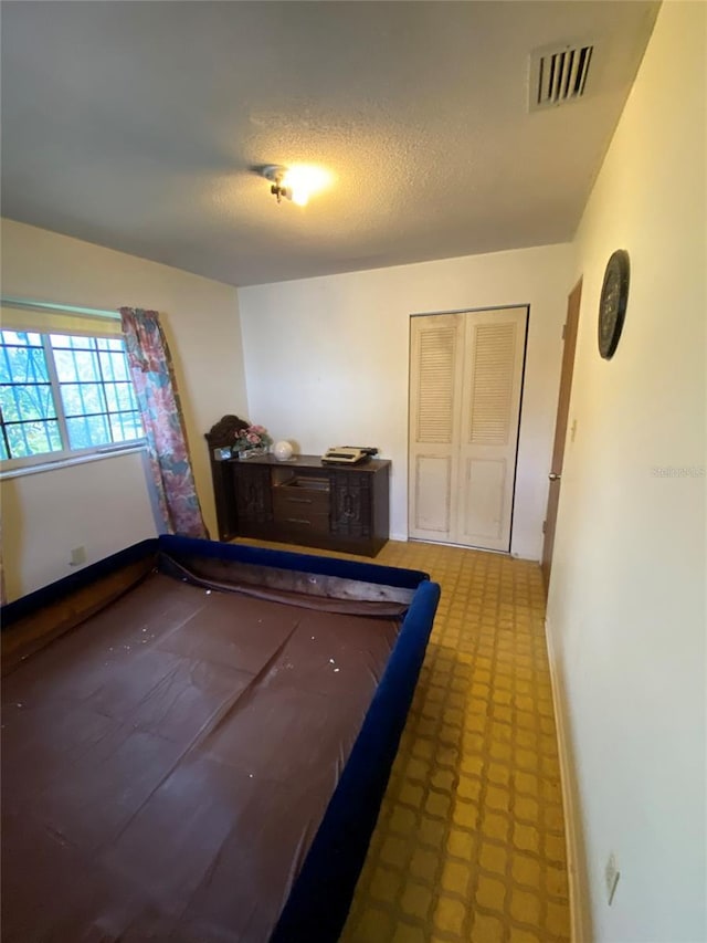 bedroom featuring a closet, visible vents, a textured ceiling, baseboards, and tile patterned floors