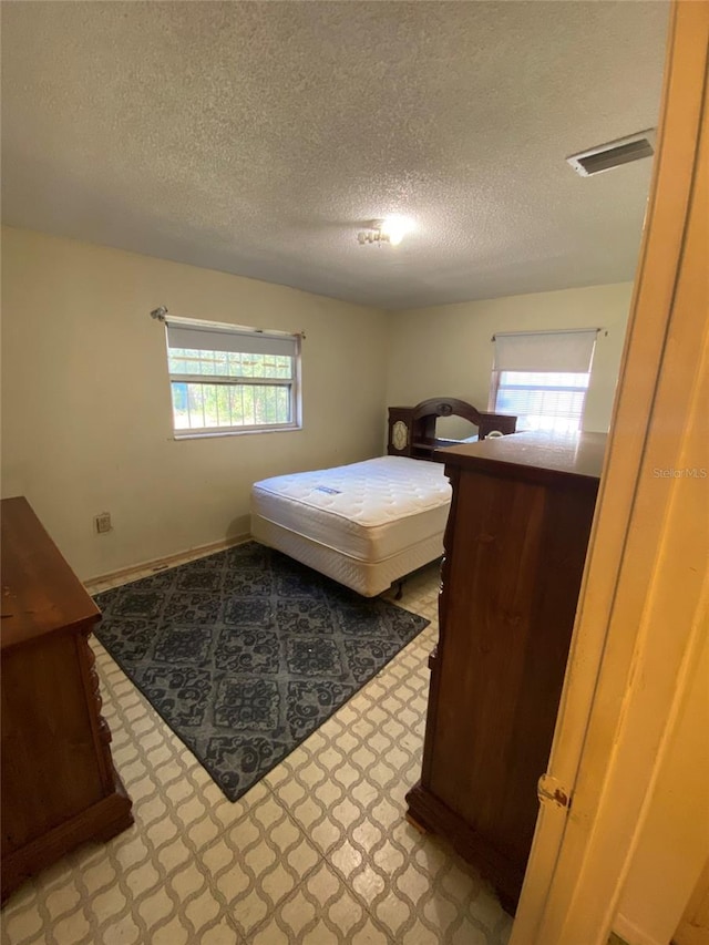 bedroom with a textured ceiling, visible vents, and baseboards