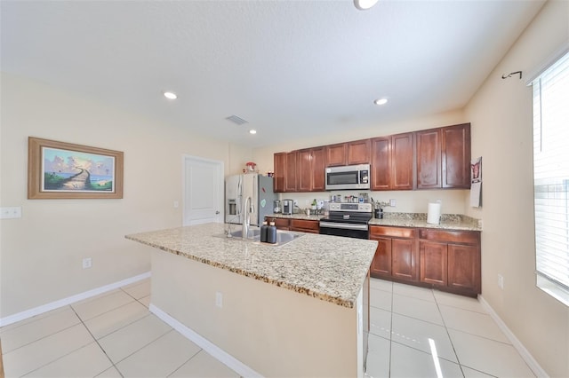 kitchen with light tile patterned floors, a center island with sink, baseboards, appliances with stainless steel finishes, and a sink