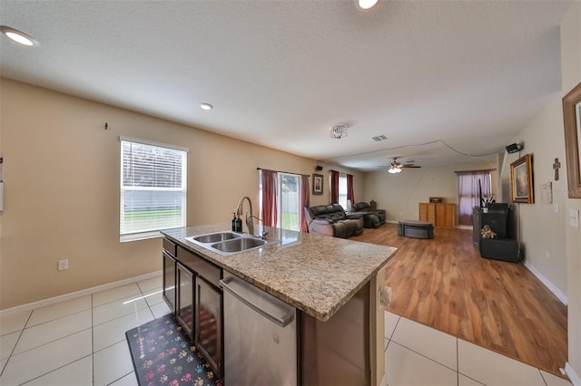 kitchen with light tile patterned floors, a ceiling fan, a sink, a kitchen island with sink, and stainless steel dishwasher