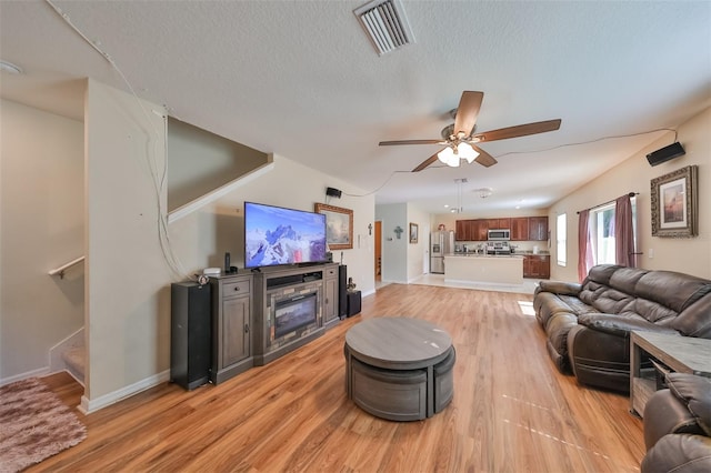 living room with ceiling fan, a textured ceiling, light wood-style flooring, visible vents, and stairs