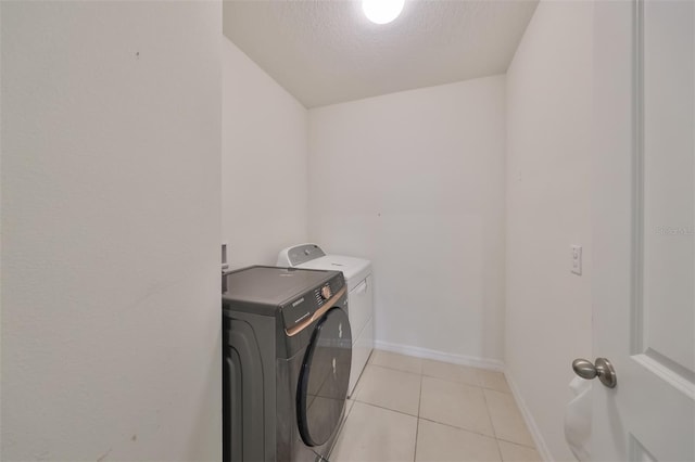 laundry area with light tile patterned flooring, a textured ceiling, laundry area, independent washer and dryer, and baseboards