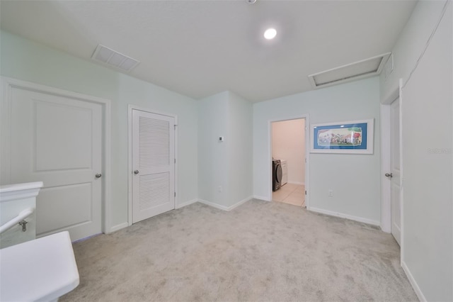 unfurnished bedroom featuring light colored carpet, visible vents, a closet, attic access, and washer / dryer