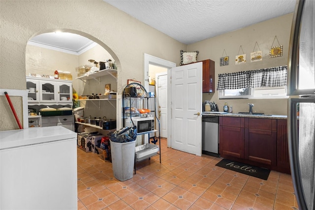 kitchen featuring a sink, a textured wall, a textured ceiling, and stainless steel dishwasher