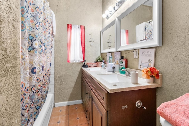 full bath featuring a textured wall, tile patterned flooring, a sink, and baseboards