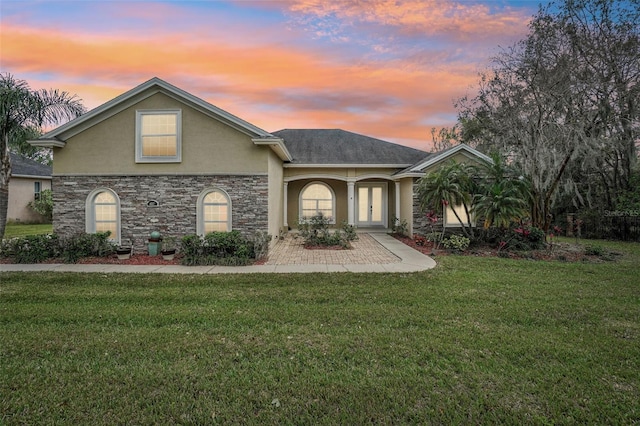 view of front of house featuring stone siding, a lawn, and stucco siding