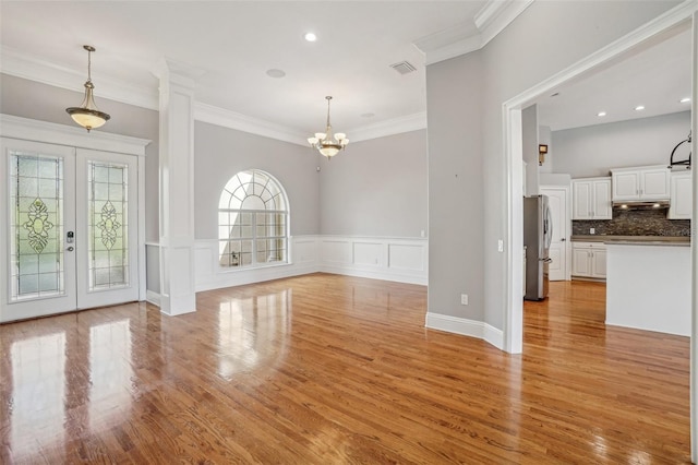 interior space with crown molding, a chandelier, a decorative wall, and light wood finished floors