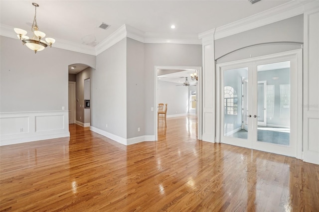 unfurnished room with visible vents, light wood-style flooring, crown molding, french doors, and a decorative wall