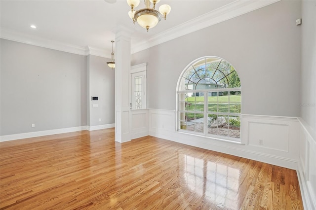 spare room featuring wainscoting, light wood finished floors, an inviting chandelier, and crown molding