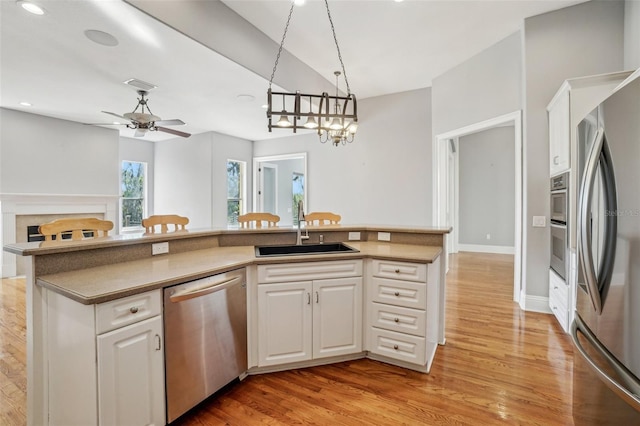 kitchen featuring stainless steel appliances, a sink, light wood-style flooring, and white cabinets