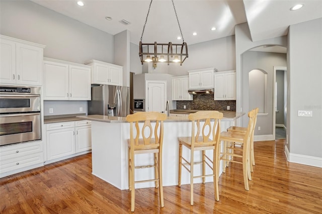 kitchen with arched walkways, a towering ceiling, appliances with stainless steel finishes, under cabinet range hood, and a kitchen bar