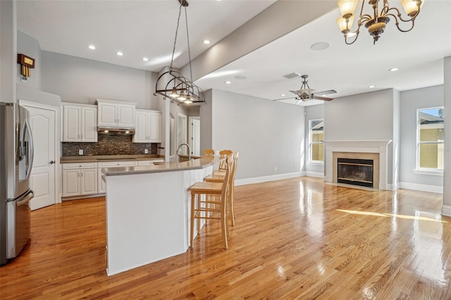 kitchen featuring visible vents, decorative backsplash, a fireplace with flush hearth, under cabinet range hood, and stainless steel fridge with ice dispenser