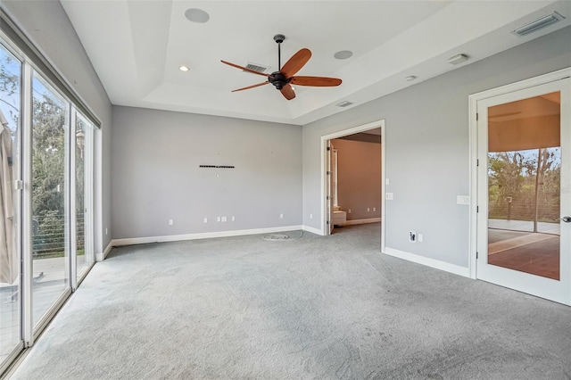 empty room with a tray ceiling, carpet, visible vents, ceiling fan, and baseboards