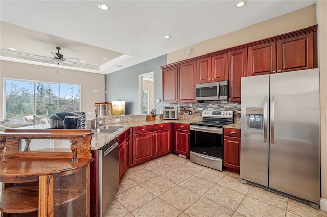 kitchen with a tray ceiling, stainless steel appliances, backsplash, a sink, and a peninsula