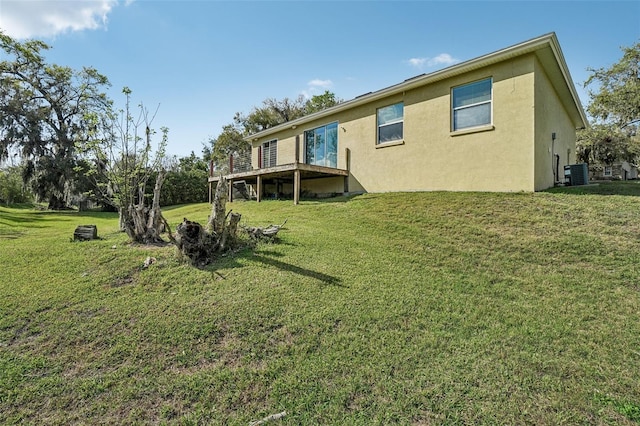 back of house featuring central air condition unit, a deck, a lawn, and stucco siding