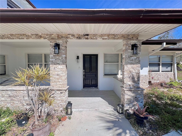 view of exterior entry with a porch, stone siding, and stucco siding