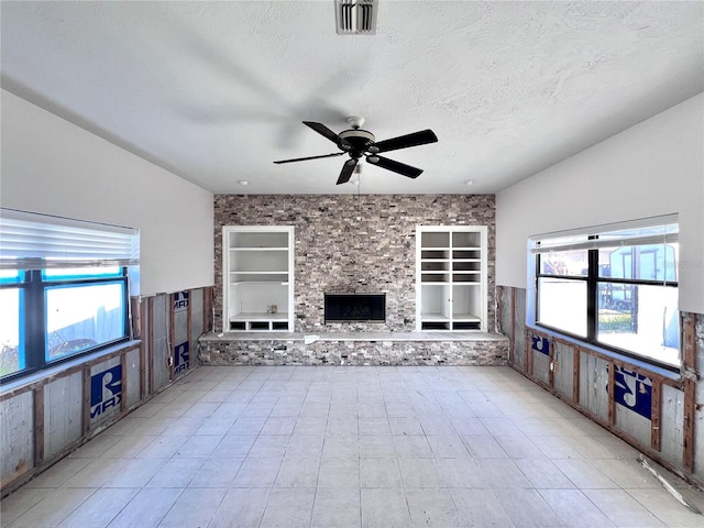 unfurnished living room featuring built in features, a healthy amount of sunlight, visible vents, and a textured ceiling