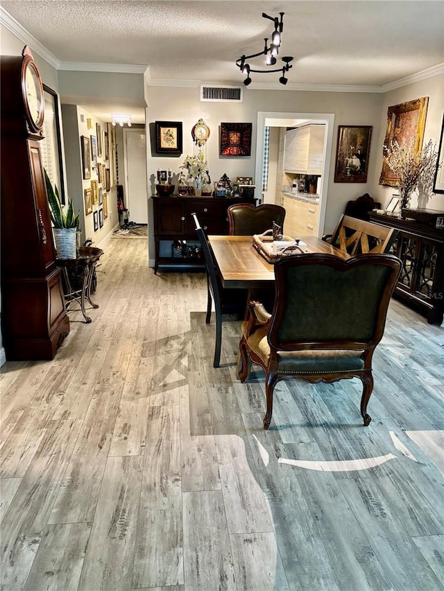 dining space featuring light wood-style flooring, a textured ceiling, visible vents, and crown molding