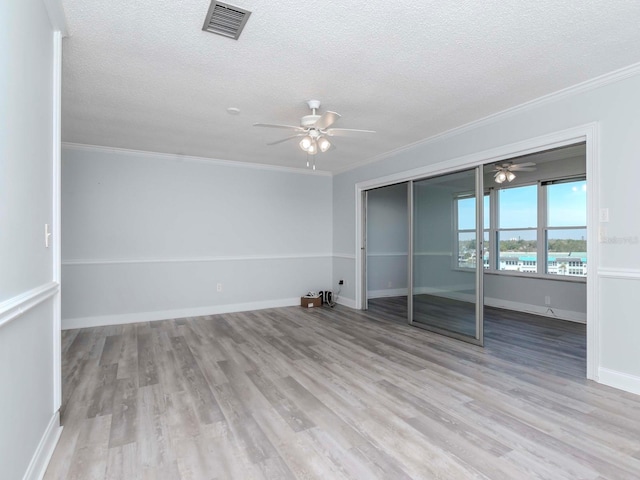 unfurnished bedroom featuring a textured ceiling, wood finished floors, visible vents, and crown molding