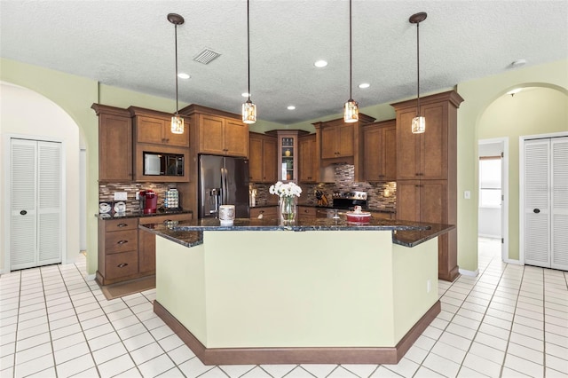 kitchen with light tile patterned floors, brown cabinetry, arched walkways, visible vents, and appliances with stainless steel finishes
