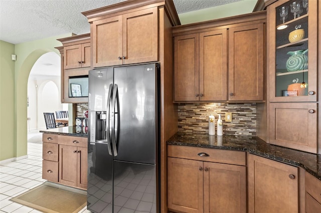 kitchen featuring tasteful backsplash, arched walkways, brown cabinetry, refrigerator with ice dispenser, and light tile patterned flooring