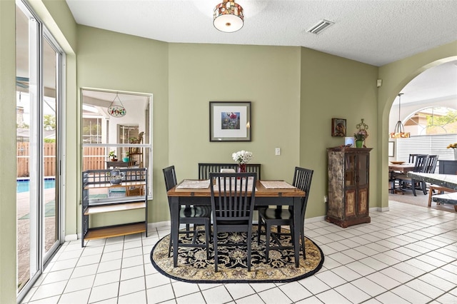 dining area featuring baseboards, light tile patterned floors, a textured ceiling, visible vents, and arched walkways