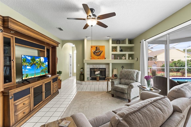 living area with a tiled fireplace, light tile patterned floors, a textured ceiling, a ceiling fan, and arched walkways