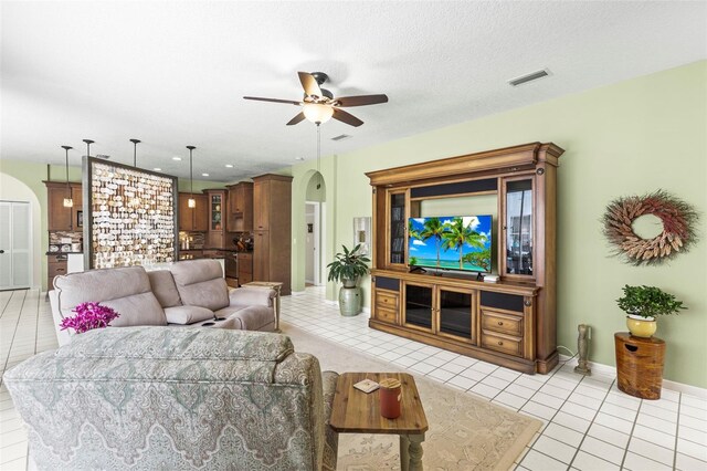 living area featuring visible vents, light tile patterned floors, baseboards, arched walkways, and ceiling fan