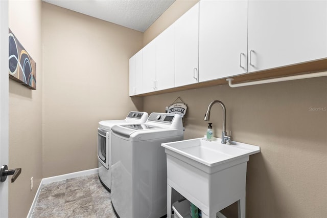 washroom with baseboards, a textured ceiling, independent washer and dryer, cabinet space, and a sink