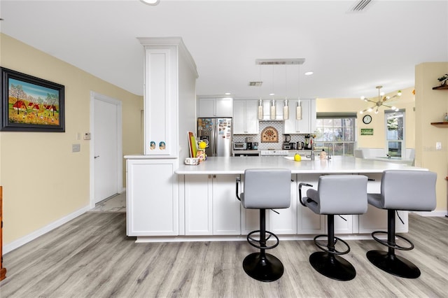 kitchen featuring tasteful backsplash, light countertops, white cabinets, light wood-type flooring, and stainless steel fridge