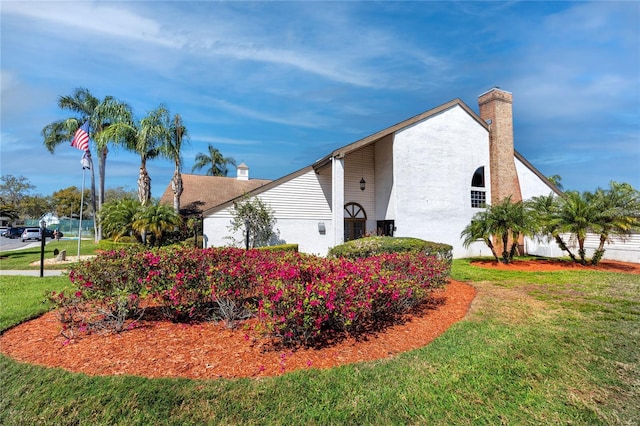 view of side of property featuring a lawn, a chimney, and stucco siding