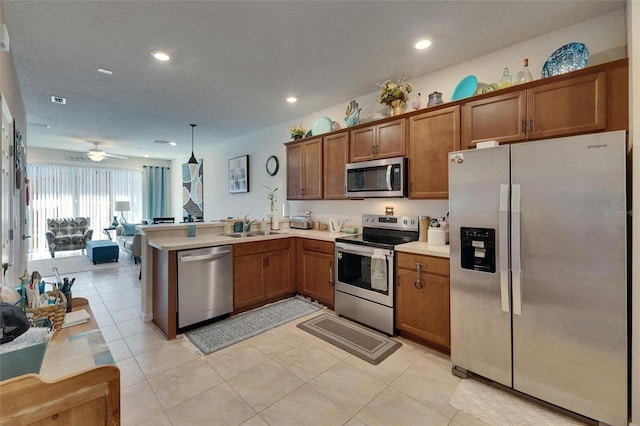 kitchen with light countertops, appliances with stainless steel finishes, brown cabinetry, open floor plan, and a peninsula